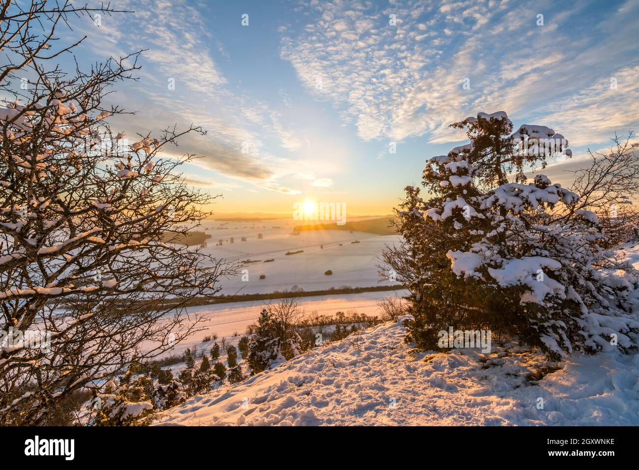 Beautiful colourful sunset over winter landscape in the Swabian Alps with trees in the foreground Stock Photo
