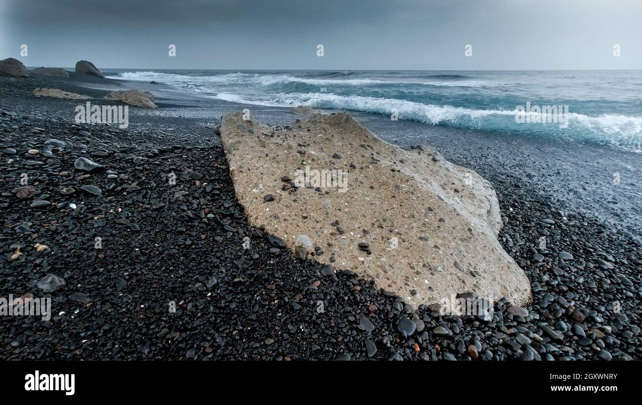 Rocks and cliffs on deserted volcanic ocean beach on cold windy day ...