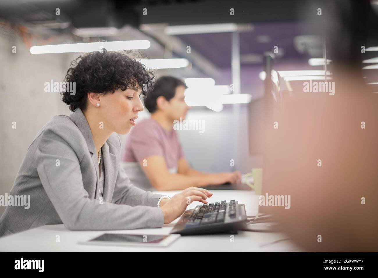young female software developer using desktop computer while writing ...