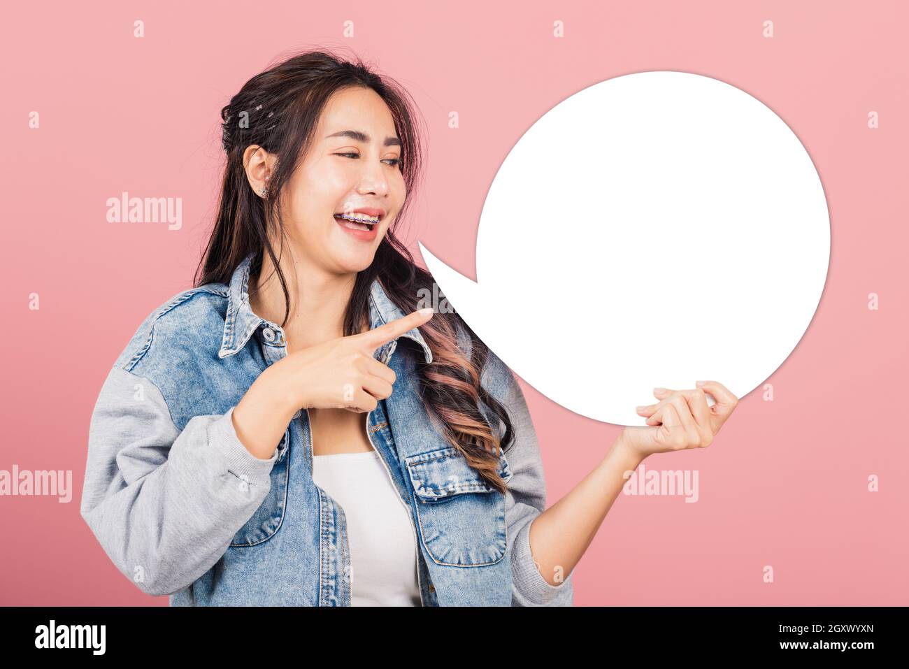 Happy Asian beautiful young woman smiling excited wear denims hold empty speech bubble sign, Portrait female posing finger pointing bubble for your te Stock Photo