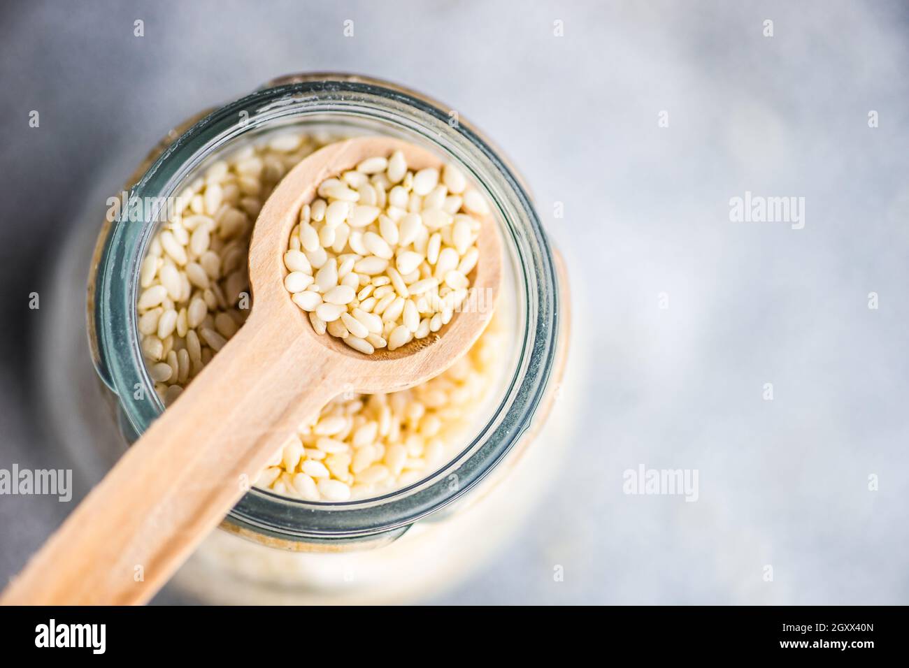 Overhead view of a glass jar of sesame seeds with a wooden spoon Stock Photo