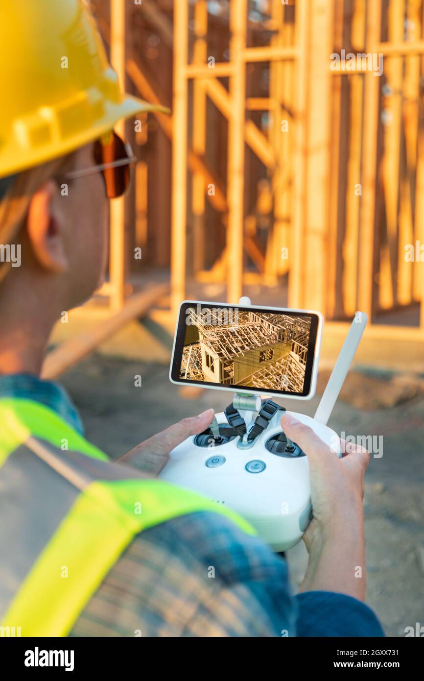 Female Unmanned Aircraft System (UAV) Quadcopter Drone Pilot with Controller Inspecting New House Framing. Stock Photo