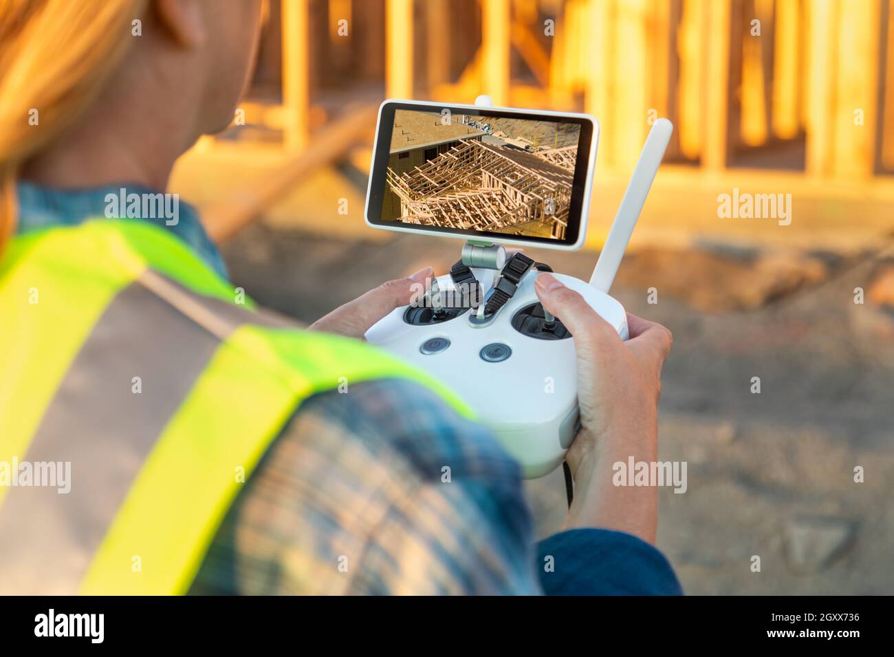Female Unmanned Aircraft System (UAV) Quadcopter Drone Pilot with Controller Inspecting New House Framing. Stock Photo