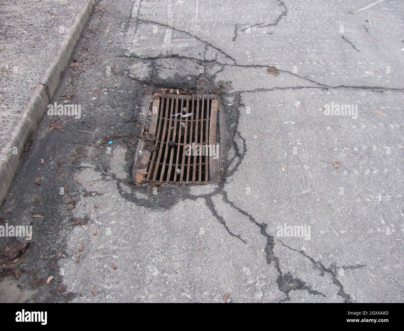 Rusty storm drain grate in cracked asphalt Stock Photo