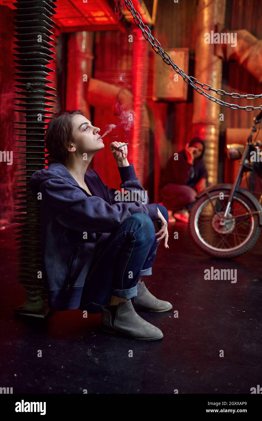 Drug addict woman with cigarette in high, shebang interior on background. Narcotic addiction problem, eternal depression of junky people Stock Photo