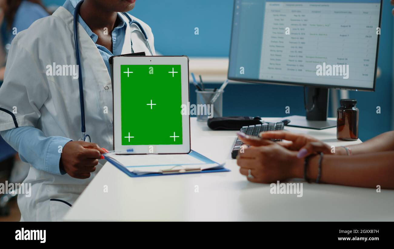 Close up of doctor vertically holding tablet with green screen on desk ...