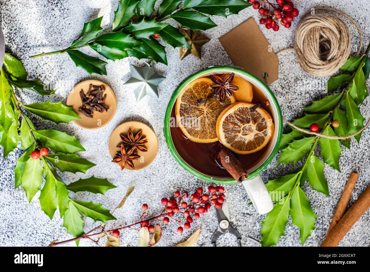 Cup of spiced mulled tea on a table with holly, spices, string, gift ...