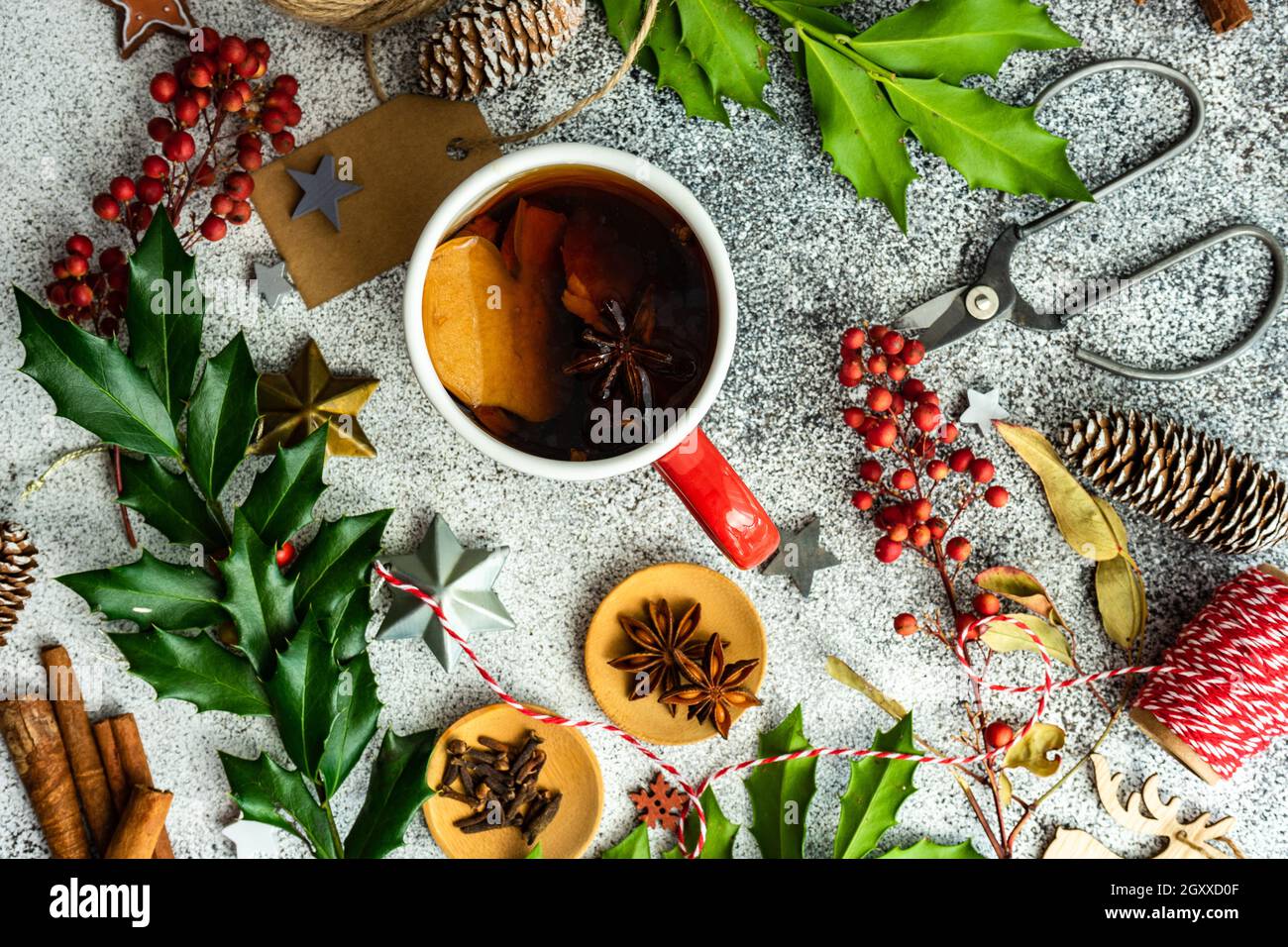 Cup of spiced mulled tea on a table with holly, spices, string, gift ...