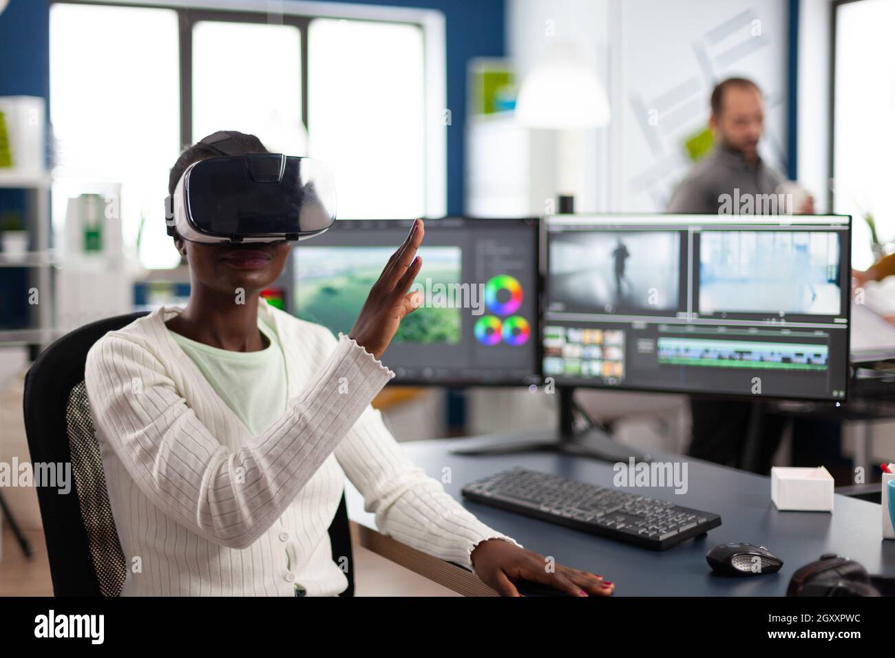 African video video maker experiencing VR headset, gesturing, editing video film montage working at footage and sound on computer with two displays. Videographer processing movie in creative agency Stock Photo