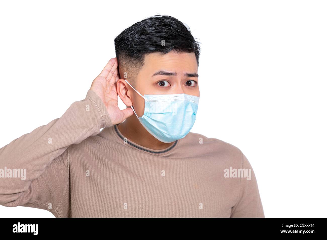 Young man wearing medical mask with hand over ear listening and hearing to rumor or gossip Stock Photo
