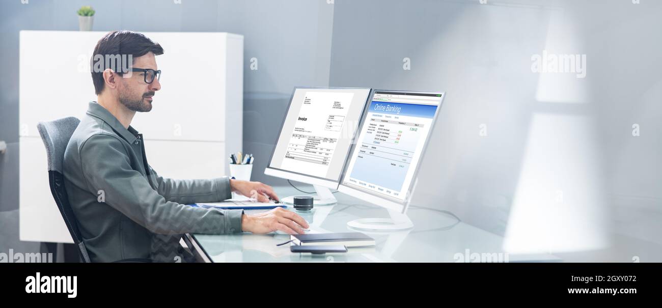 Young Businessman Looking At Invoice While Doing Online Banking On Computer Stock Photo