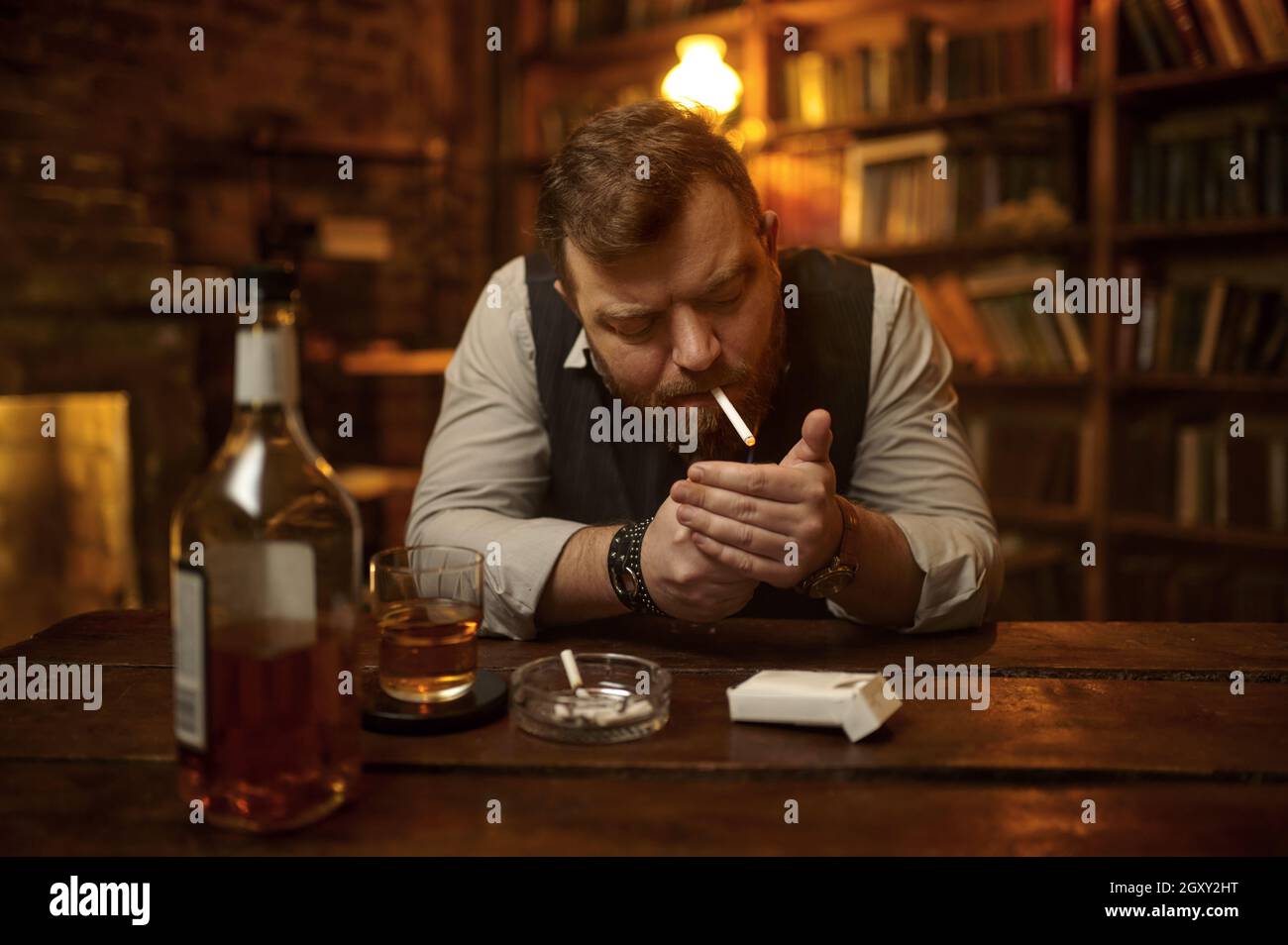 Man smokes cigarette and drinks alcohol beverage, bookshelf and rich