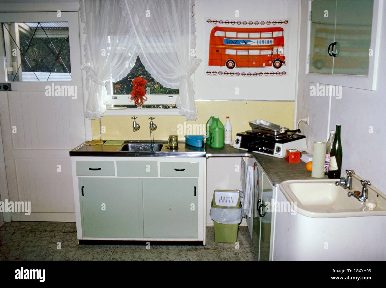A very basic kitchen in an appartment or flat in a suburb of Sydney, NSW, Australia in 1973. Interestingly although it is poorly equiped (with only a small plug-in, worktop hob and grill) it contains two sinks! For decoration there is a tea-towel of a London bus pinned to the wall This image is from an old amateur Kodak colour transparency – a vintage 1970s photograph. Stock Photo