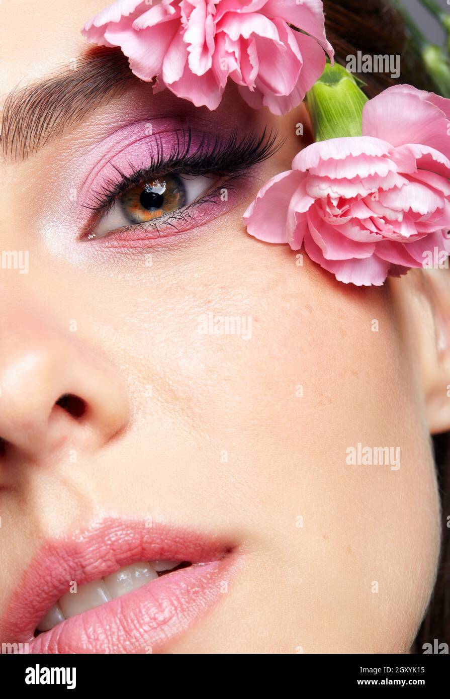 Closeup macro shot of human female face. Woman with natural face and eyes beauty makeup. Pink carnation flowers on the temple. Stock Photo