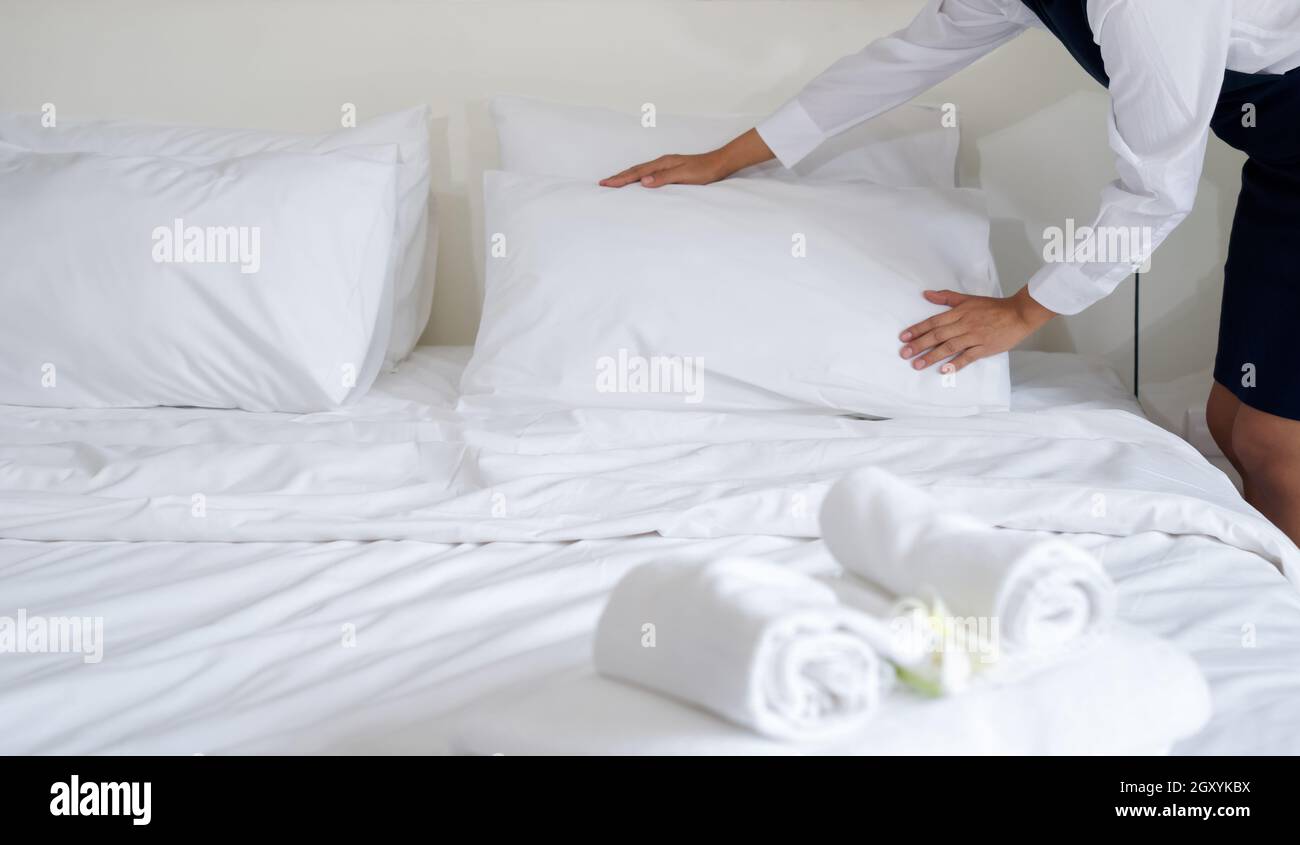Young hotel maid making the bed. Hotel staff in blue uniform preparing