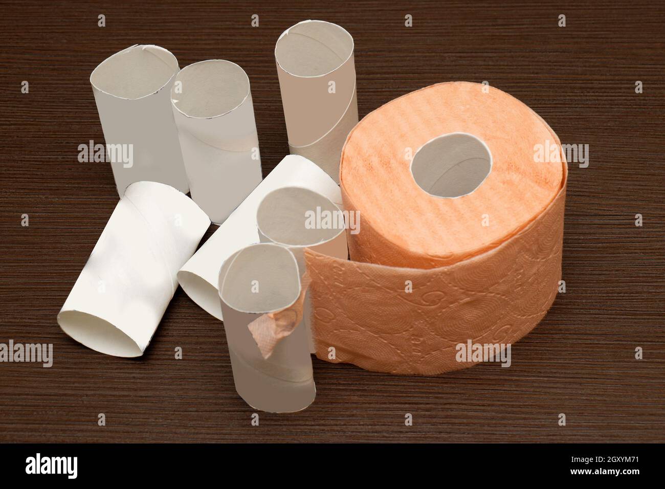 Used toilet paper rolls pile with one still in use on wooden table