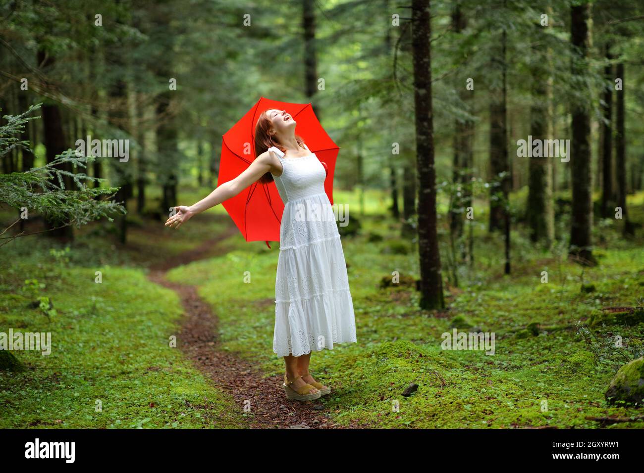 Excited woman with red umbrella celebrating vacation in a forest under ...