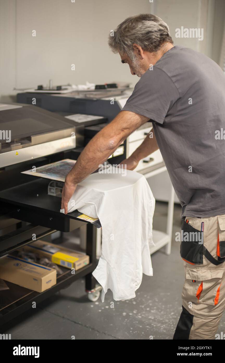 Professional graphic print technician work on digital t-shirt printing machine printer in printing production shop Stock Photo