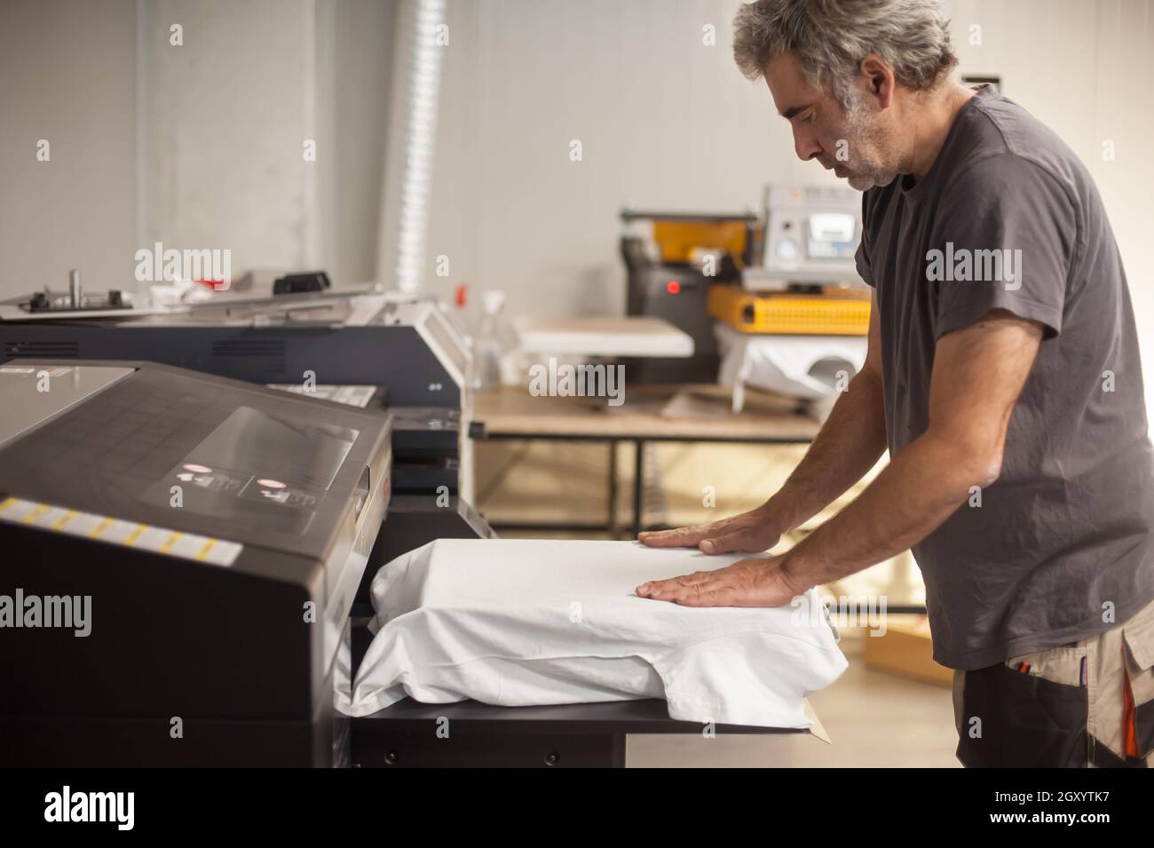 Professional graphic print technician work on digital t-shirt printing machine printer in printing production shop Stock Photo