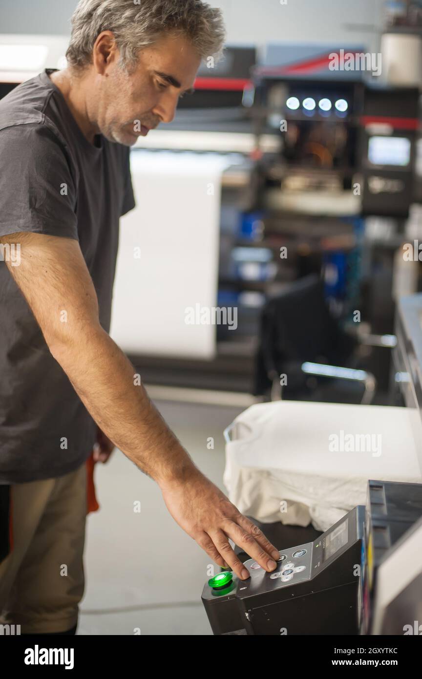 Professional graphic print technician work on digital t-shirt printing machine printer in printing production shop Stock Photo