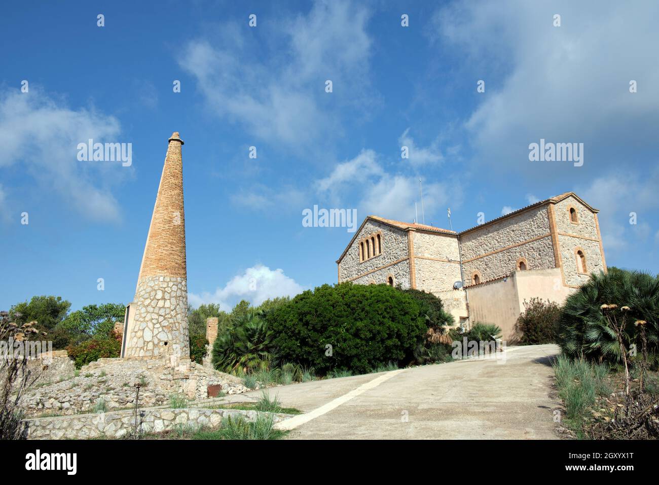 Typical Catalan architecture house built in stone and brick with a wall and hanging plants. Obelisk of the same construction material as the house. Stock Photo