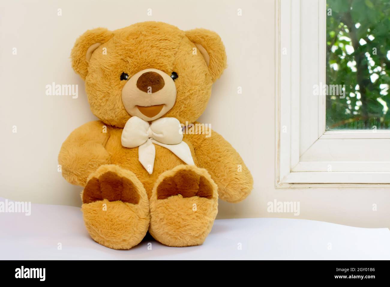 Teddy bear sitting on a bed near a window Stock Photo - Alamy