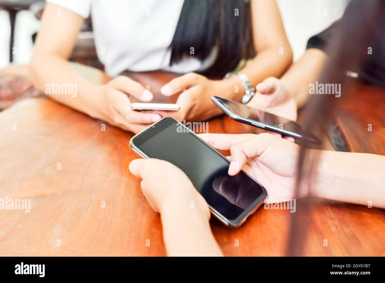 Unidentified three young people using  smartphone together. In selective focus.Close-up. Technology gadget and phone addiction concept. Stock Photo