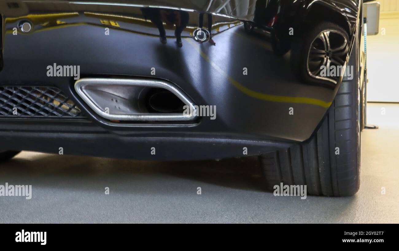Square tailpipe at the rear right side of a black sports car. Very low plan. The rear bumper, wheel and tailpipe of the packed vehicle are smoke- and Stock Photo