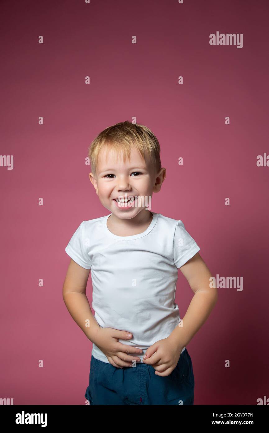 Caucasian boy 3 years old makes faces while looking at camera on pink background. Stock Photo