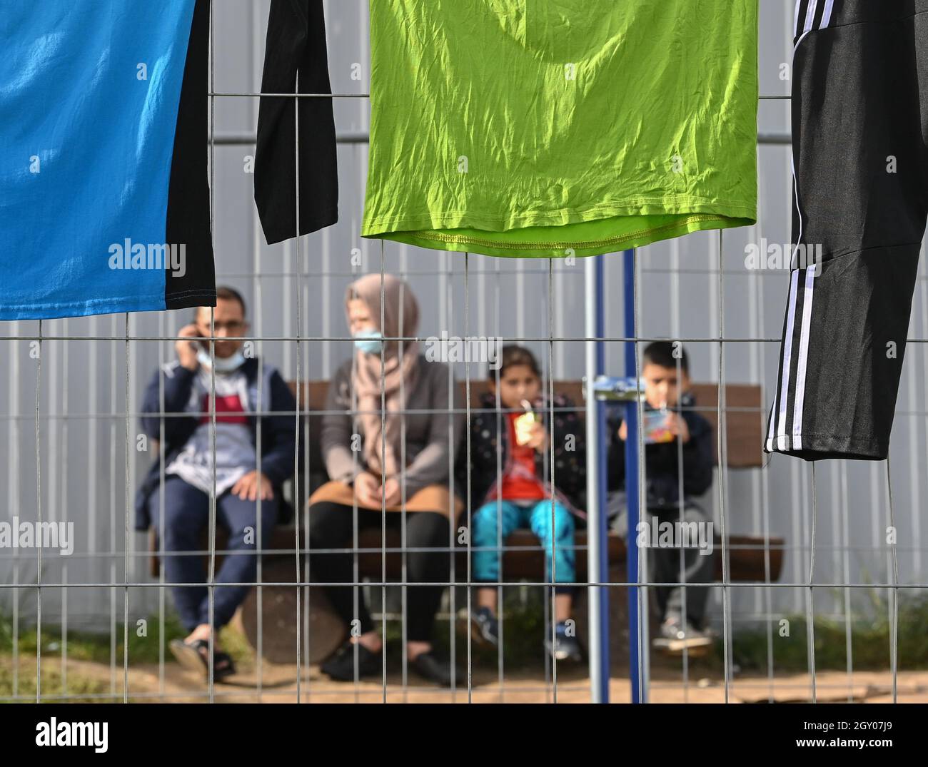 06 October 2021, Brandenburg, Eisenhüttenstadt: Migrants sit behind a fence at the Central Initial Reception Facility for Asylum Seekers (ZABH) in the state of Brandenburg. In the course of the significant increase in the registration of migrants in Brandenburg, the Minister of the Interior of Brandenburg, Stübgen (CDU), informed himself about the current situation on site. Photo: Patrick Pleul/dpa-Zentralbild/ZB Stock Photo