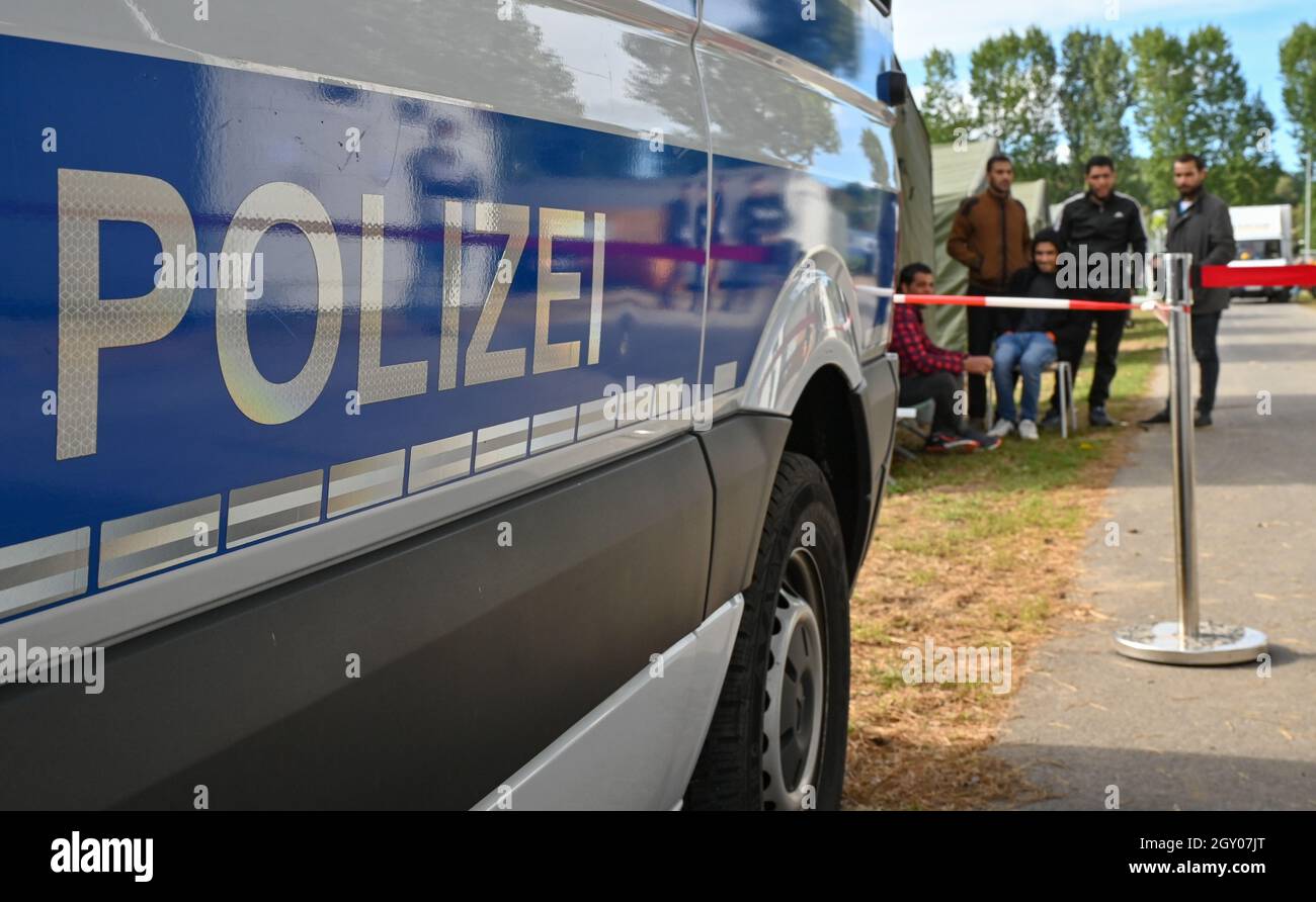 06 October 2021, Brandenburg, Eisenhüttenstadt: A police vehicle stands in front of migrants at the Central Initial Reception Facility for Asylum Seekers (ZABH) in the state of Brandenburg. In the course of the significantly increased registration of migrants in Brandenburg, the Minister of the Interior of Brandenburg, Stübgen (CDU), informed himself about the current situation on site. Photo: Patrick Pleul/dpa-Zentralbild/ZB Stock Photo