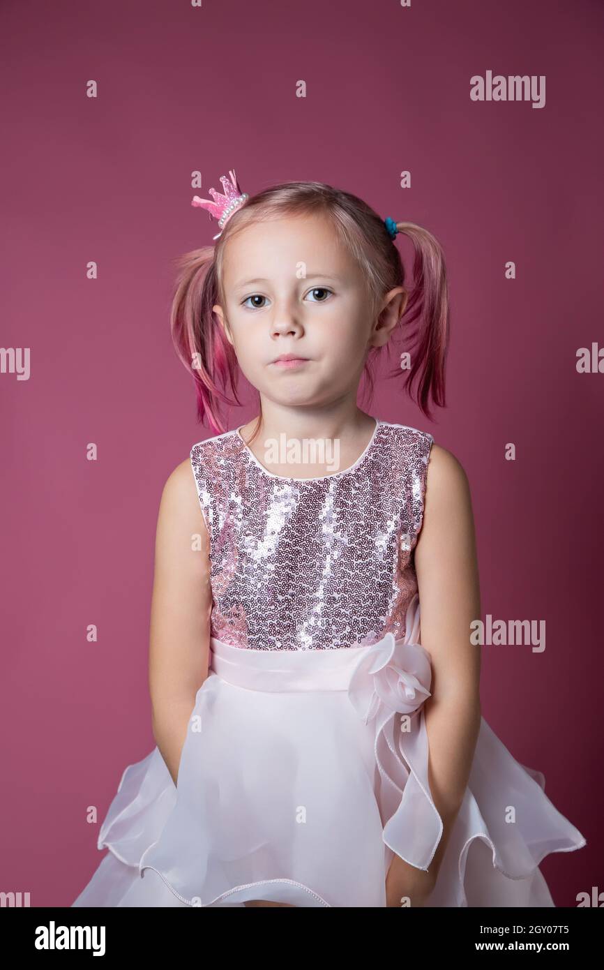Little caucasian girl in a festive dress with sequins posing like a princess on a pink background looking at the camera Stock Photo