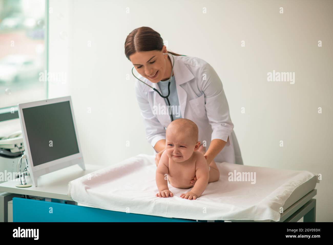 Experienced doctor examining an upset infant with a sterile stethoscope Stock Photo