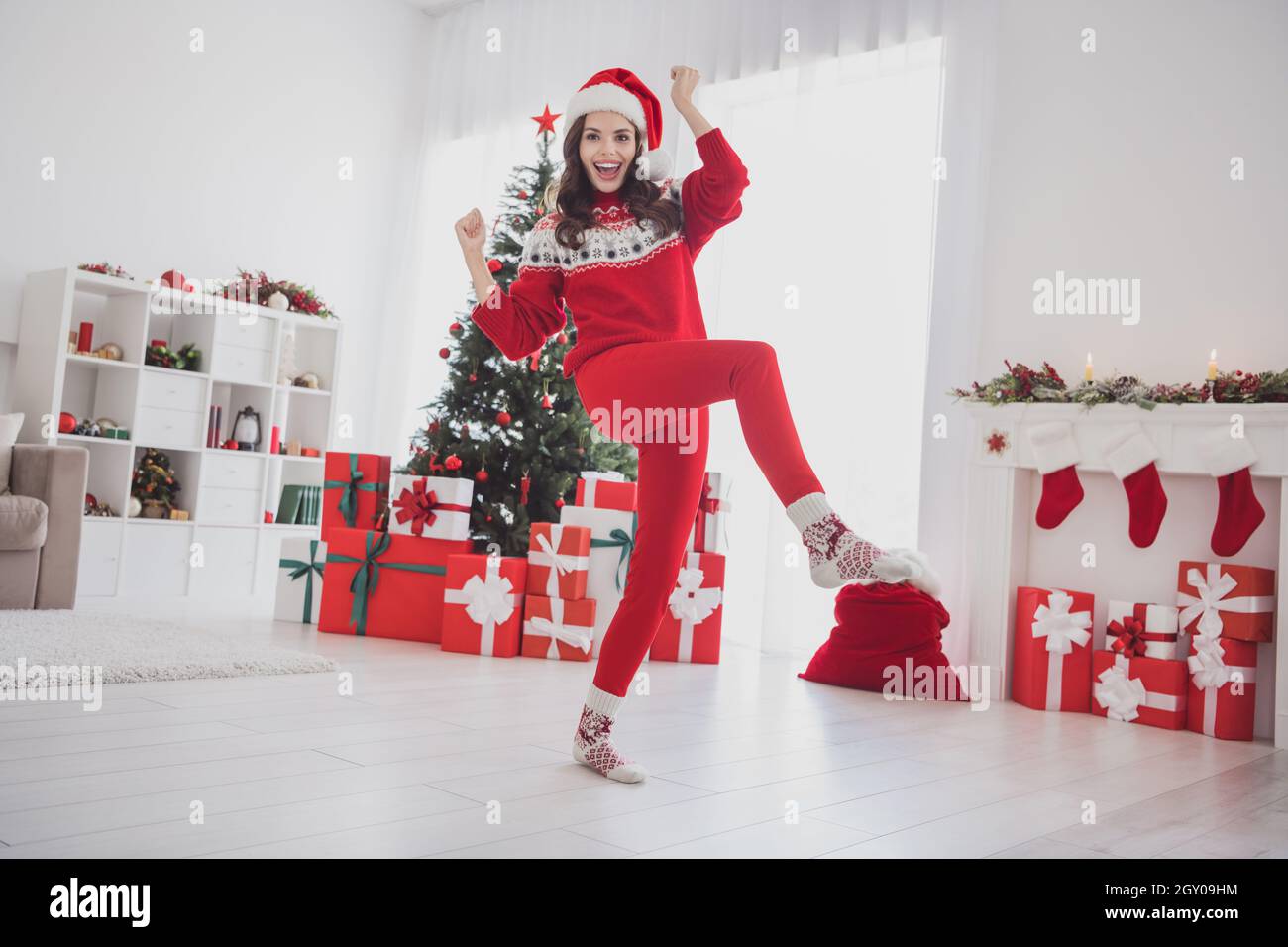 Photo of astonished crazy lady raise fists attain goal wear santa hat sweater pants socks in decorated home indoors Stock Photo