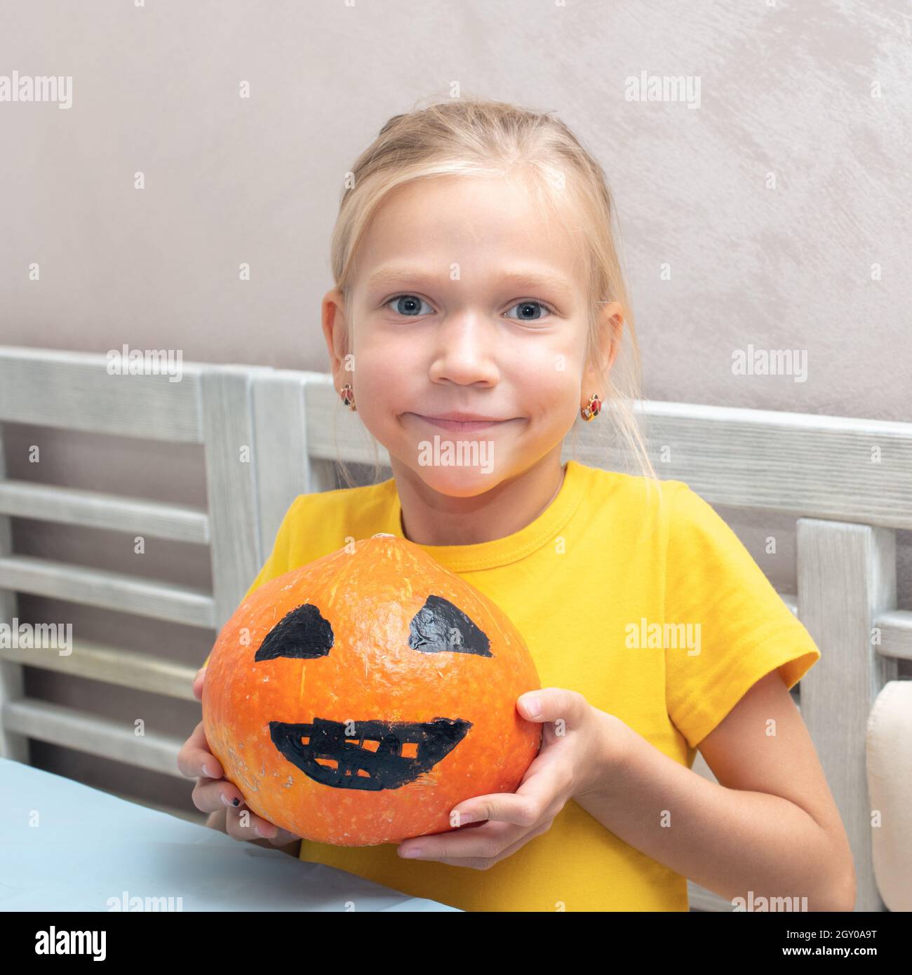 The girl shows a pumpkin with a painted scary face, creating a Halloween Jack Lantern. Halloween party and family lifestyle background Stock Photo