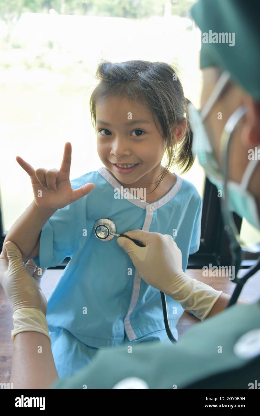 Asian doctorin surgical gown examining a little patient girl  by stethoscope in office. Medicine and health care concept. Stock Photo