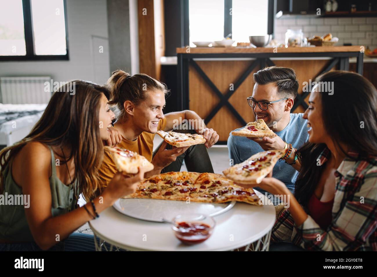 laughing friends eating pizza and having fun. They are enjoying eating and  drinking together Stock Photo