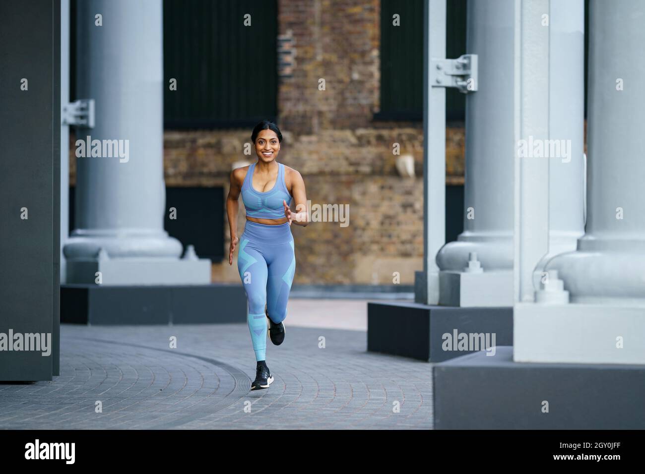 Woman in a grey outfit running in urban setting Stock Photo