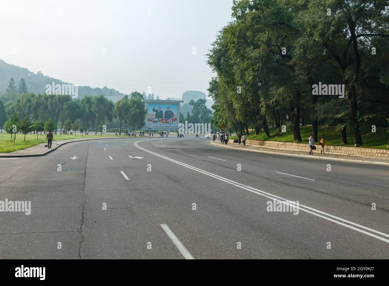 Pyongyang, North Korea - July 28, 2014: An empty road on a street in Pyongyang. A panel depicting North Korean leaders Kim Il Sung and Kim Jong Il on Stock Photo