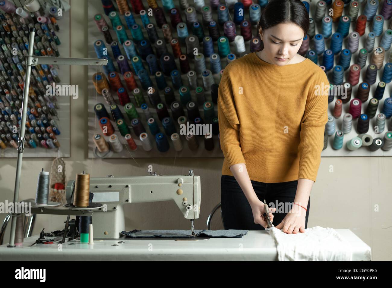 A Caucasian dressmaker stands at a work table and cuts white fabric