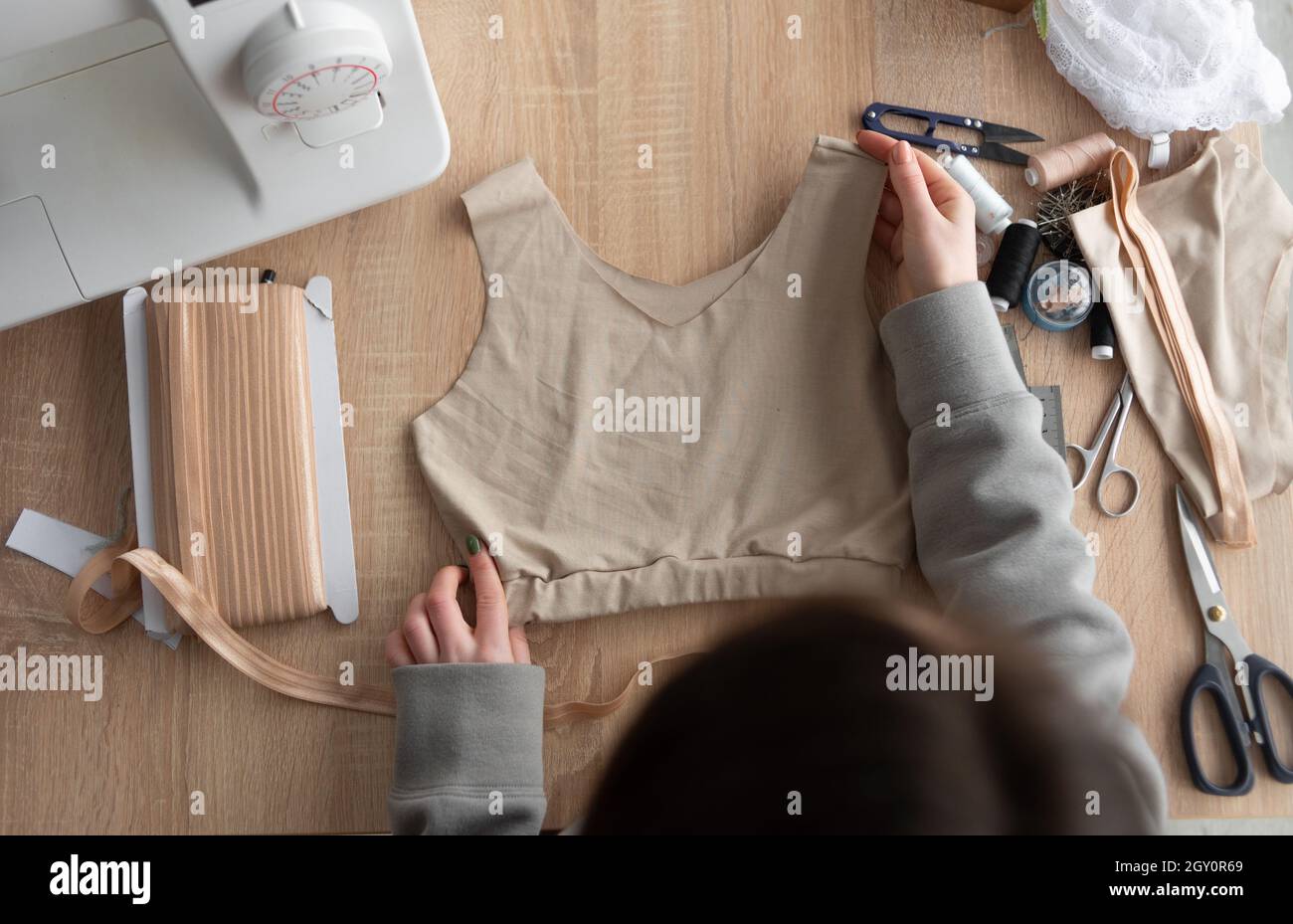 top view of the workplace of a seamstress or fashion designer. the woman works sews a sports women's T-shirt. Stock Photo