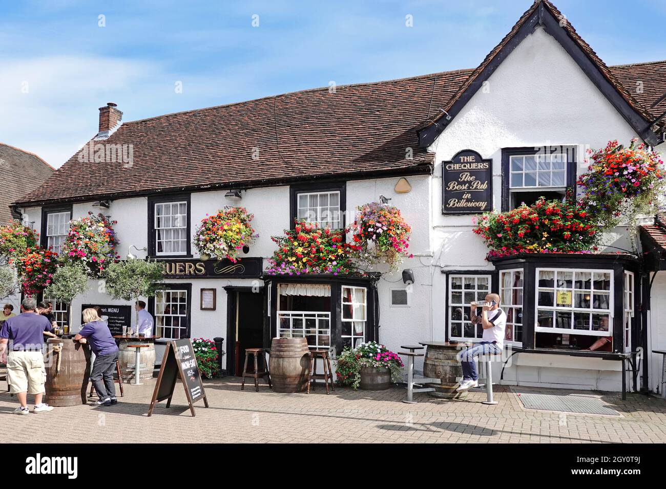Colourful summer flower displays on front old historical Chequers pub façade customers having drinks at wooden beer barrel tables Billericay Essex UK Stock Photo