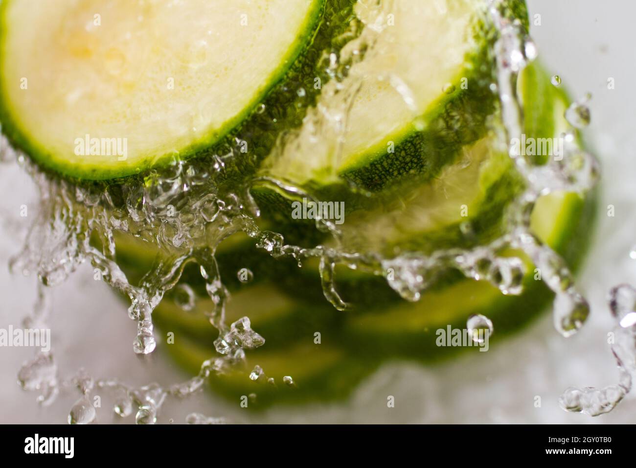 Cucumber slices stacked vertically splashed with water on a white background Stock Photo
