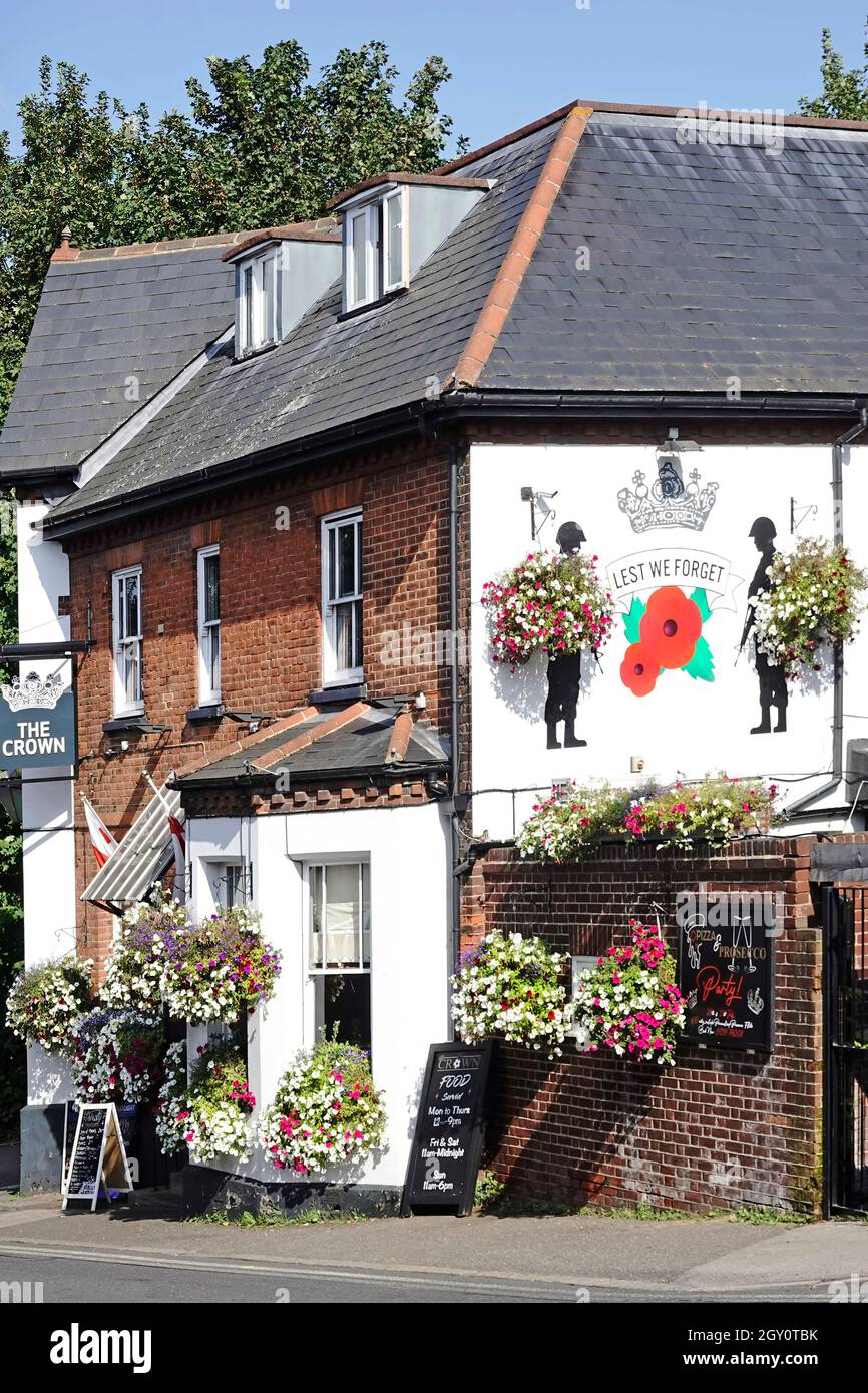 Summer hanging basket flower displays at The Crown public house with a Lest We Forget poppy & soldiers mural painted on wall High Street Billericay UK Stock Photo