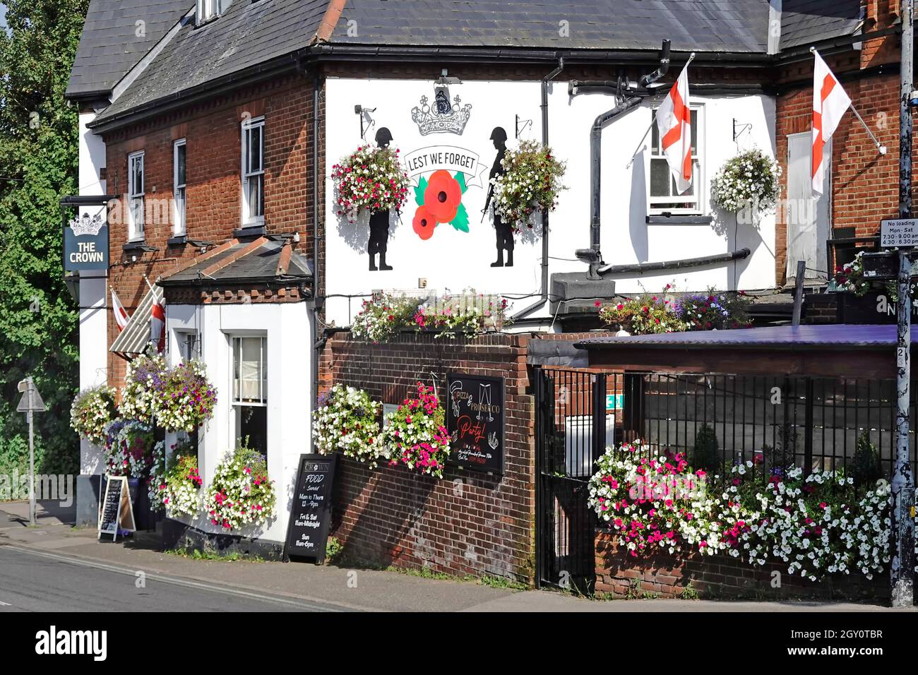 Summer hanging basket flower displays at The Crown public house with a Lest We Forget poppy & soldiers mural painted on wall high street Billericay UK Stock Photo