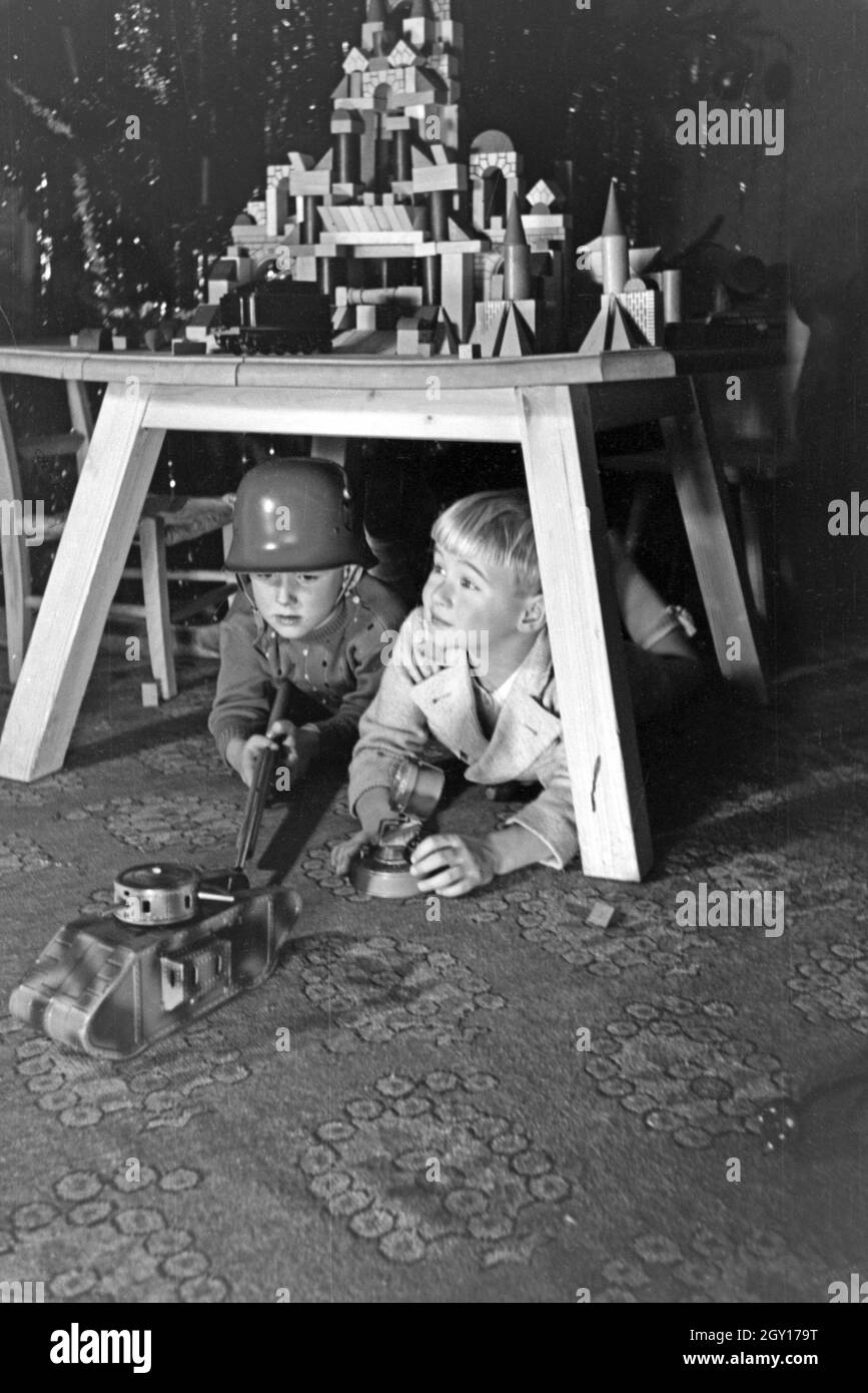 Zwei Jungen spielen am Weihnachtsabend mit Stahlhelm und Gewehr Soldaten, Deutschland 1938. Two boys playing soldiers with a steel helmet and a toy rifle under the christmas tree, Germany 1930s Stock Photo