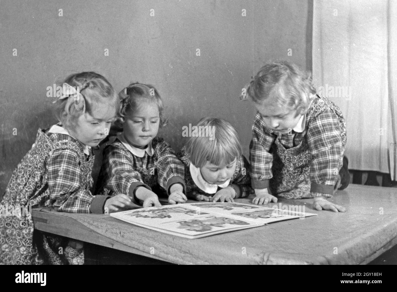 Die Knipser Vierlinge betrachten ein Bilderbuch, Deutschland 1930er Jahre. The Knipser's quadruplet girls with a storybook, Germany 1930s. Stock Photo