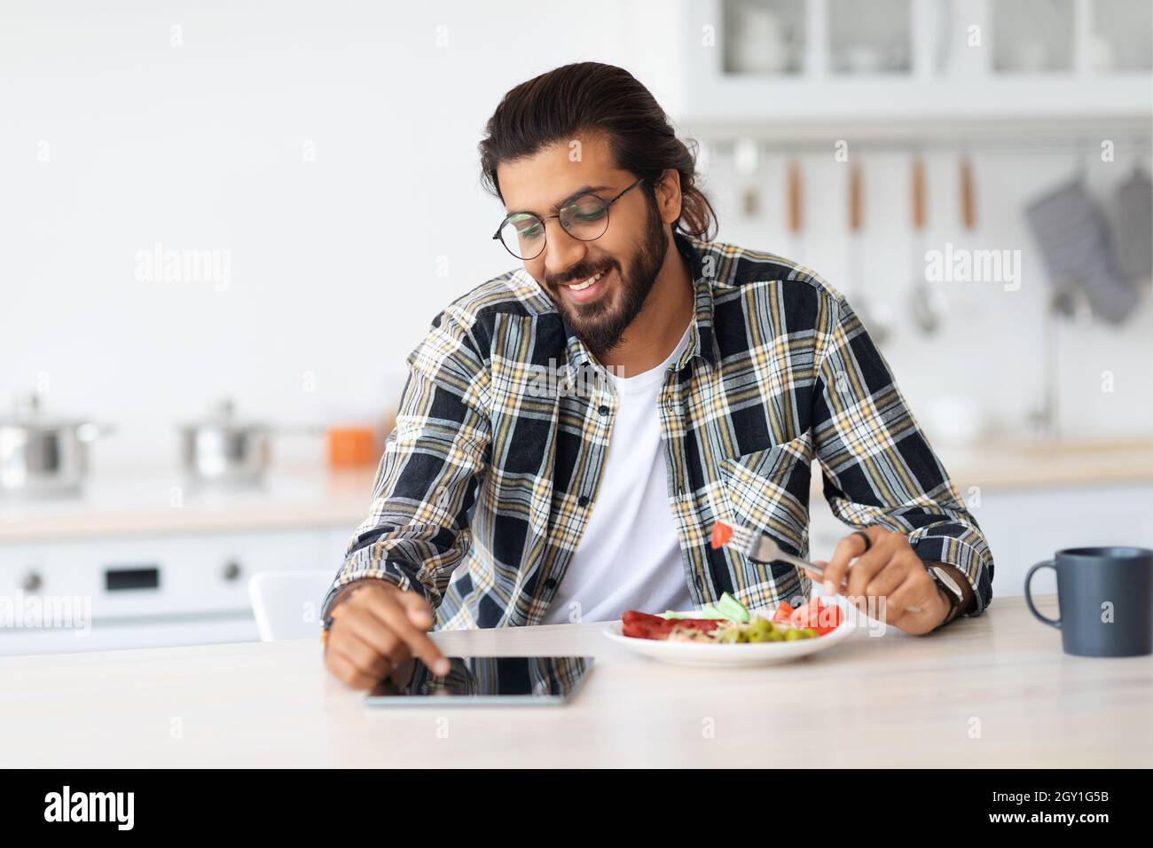 Positive arab guy having breakfast, using digital tablet, copy space Stock Photo