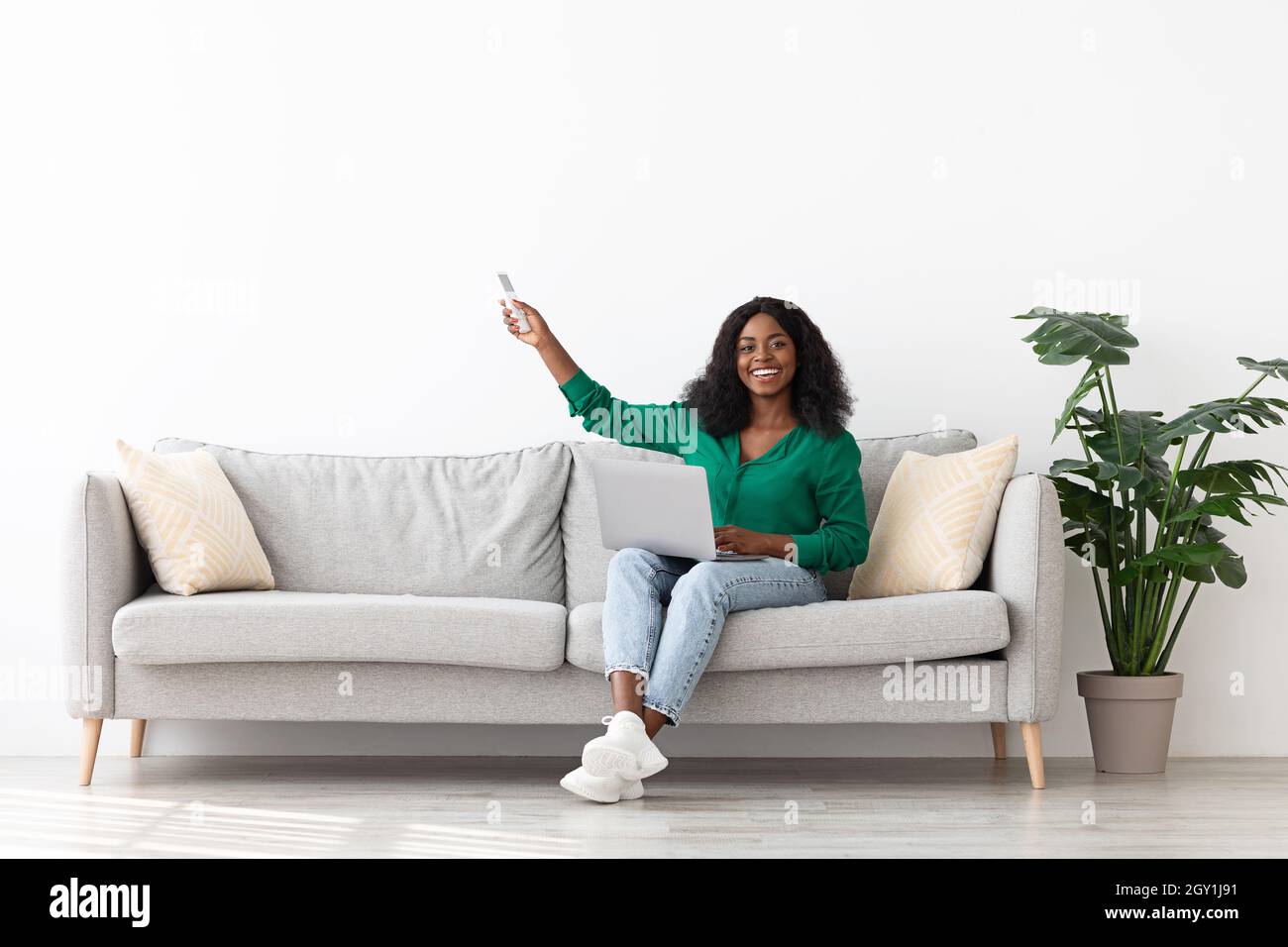 Happy black woman sitting on couch with laptop, holding remote Stock ...