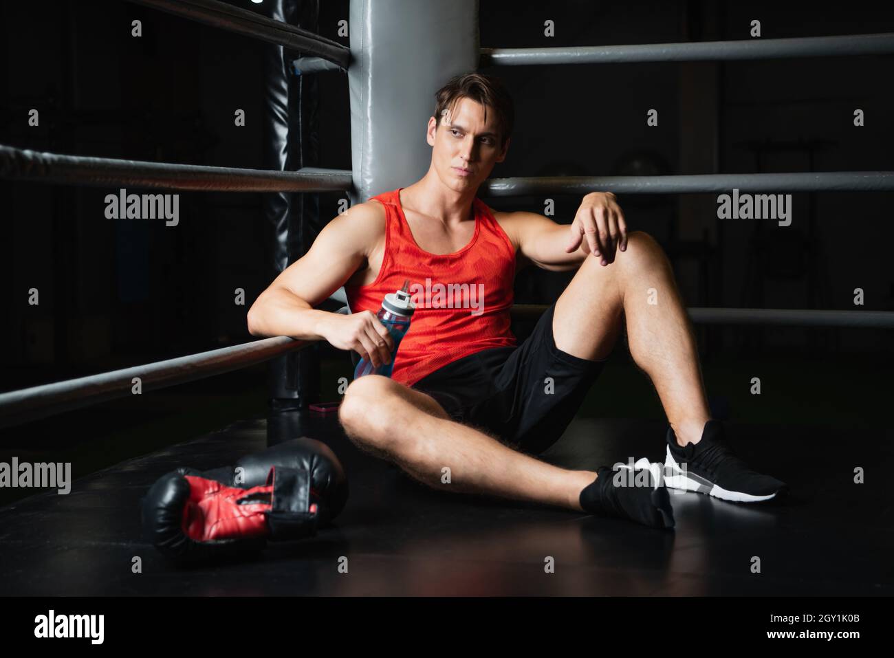 athletic man with sports bottle resting in corner of ring near boxing gloves Stock Photo